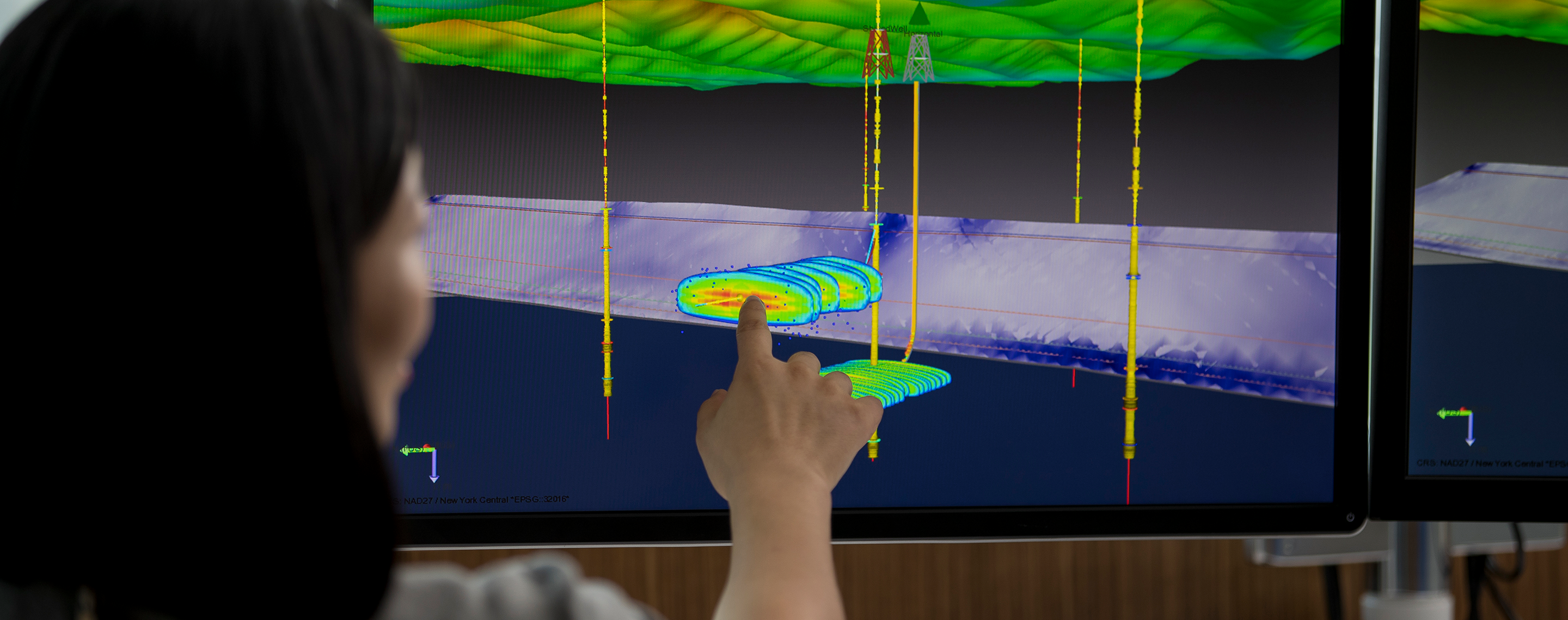 Photo of woman pointing at computer screen with microseismic rendering