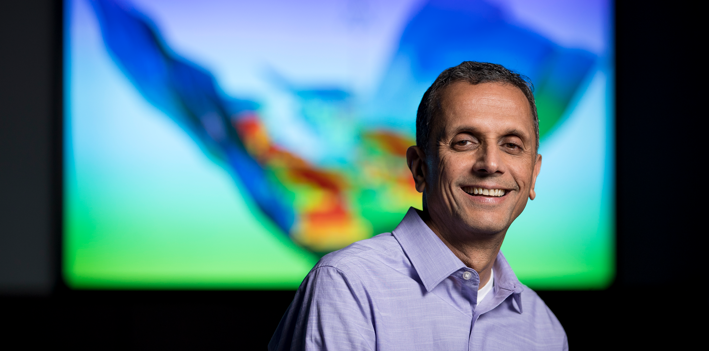 Man smiling in front of a digital screen.